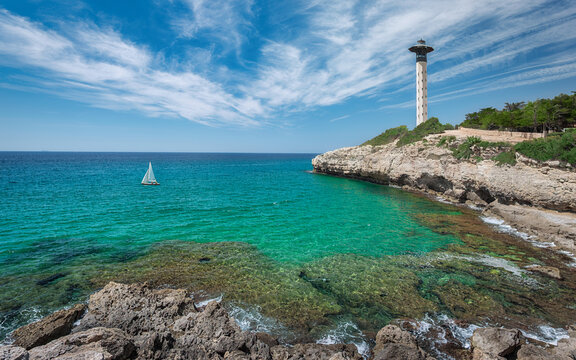 Lighthouse, Sailboat and Cliffs in Torredembarra on a Shore of The Mediterranean Sea. Tarragona, Catalonia, Spain.