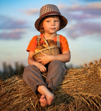 Boy with basket of buns in the background of haystacks in summer field 