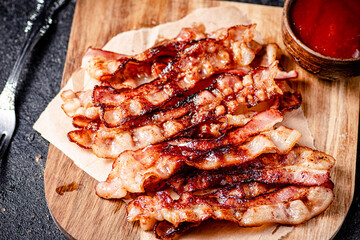 Pieces of fried bacon on a wooden cutting board. 