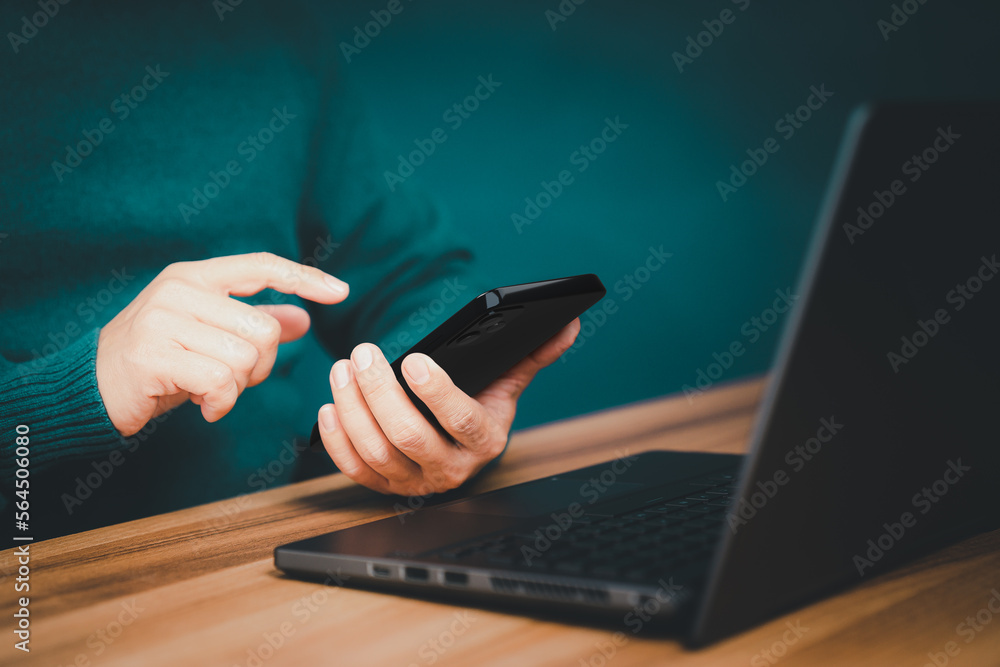 Poster Male hand using a smartphone while working on computer laptop at office for investment analyzing company financial report balance with mobile phone. Concept of people are working with mobile devices.