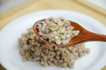 boiled green buckwheat on a white plate with a wooden spoon