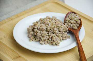 boiled green buckwheat on a white plate with a wooden spoon