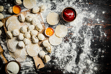 Raw dumplings on a cutting board with egg and flour. 