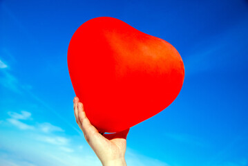 Fototapeta premium The girl holds the ball in the form of a heart against the blue sky 