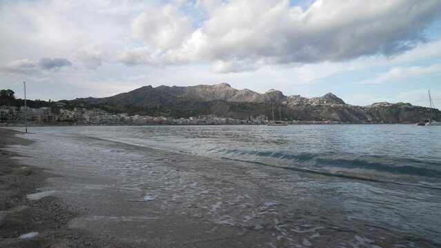 Waves lapping on beach in Bay of Naxos with Castelmola and Taormina in background, Messina, Sicily