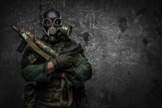 Shot of contemporary soldier with gas mask holding rifle and pistol in cross.