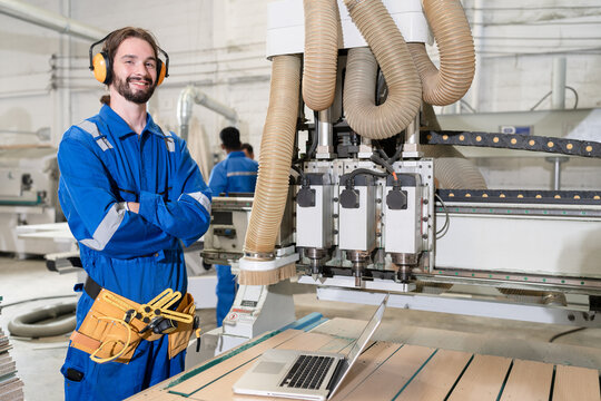 Handsome caucasian carpenter in safety blue uniform with machine at wood factory	