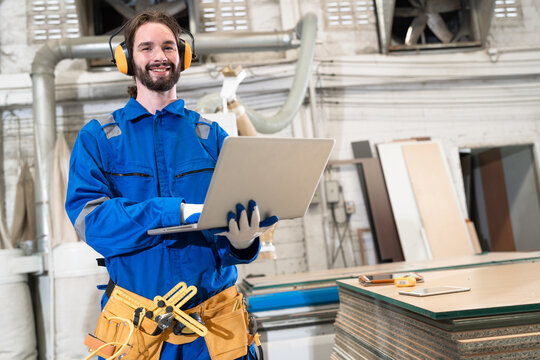 Handsome caucasian carpenter in safety blue uniform use notebook computer and checking machine at factory	