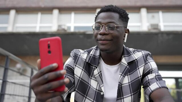 Young African man using mobile phone and earphones for online video call