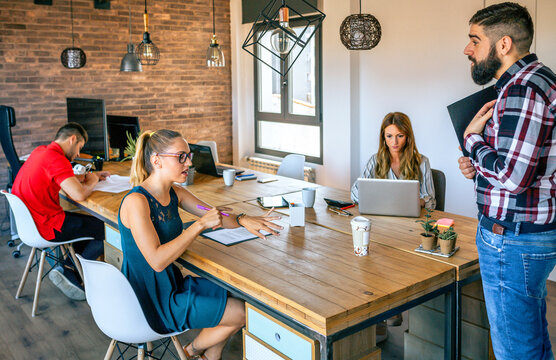 Angry Young Female Manager Pointing At Watch While Discussing With Beard Man For Coming Late To Office In The Morning. Employee Punctuality At Work Concept.