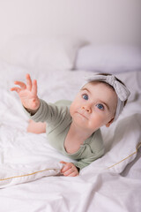 a girl with beautiful big eyes is rubbing the baby at home on the bed in a cotton bodysuit on white bed linen