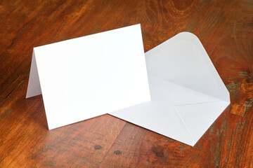 Standing blank empty rectangular greeting card and envelope mock up on dark wooden background. For...