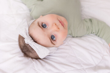 a girl with beautiful big eyes is rubbing the baby at home on the bed in a cotton bodysuit on white bed linen