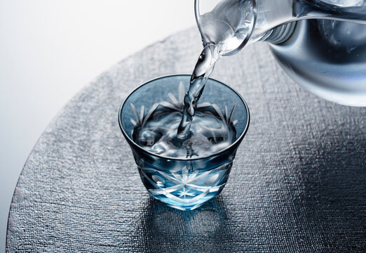 Sake poured into a faceted glass against a black background.