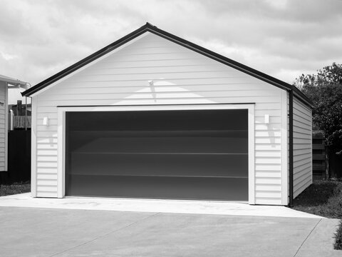 Double detached white garage with black tilt-up retractable raised panel metal door and gable metal roof