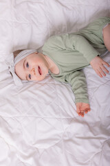 a girl with beautiful big eyes is rubbing the baby at home on the bed in a cotton bodysuit on white bed linen