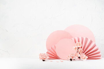 Spring stage with pink sakura flowers, pink circles, paper fans in sunlight in traditional japanese style in white interior, mockup for presentation cosmetic products, goods, design, card, poster.