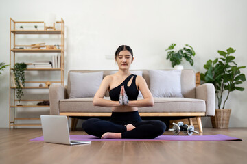 Millennial Asian woman meditating with trainer online on laptop at home