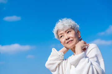 青空の下でストレッチをするシニアの女性