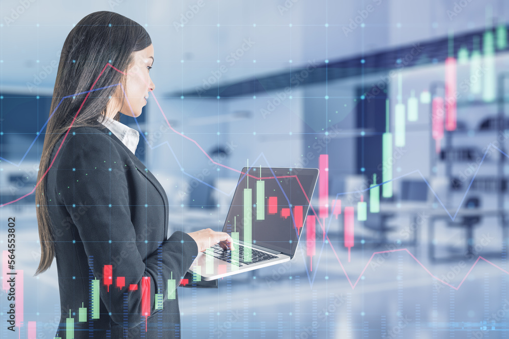 Wall mural Young caucasian woman using laptop with glowing forex chart on blurry office interior background. Trade, finance and invest concept. Double exposure.