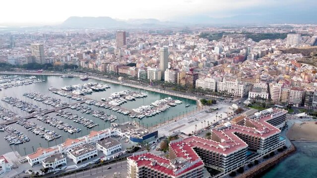 ALICANTE , Spain - December 4 2022: Cinematic footage of Alicante Marina. Aerial perspective of the city center and the touristic port. Luxury boats and yachts docked. Sunset at skyline. Truck right