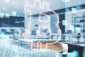 Close up of hand holding cellphone with glowing bitcoin hologram on blurry office interior background. Cryptocurrency, money and finance concept. Double exposure.