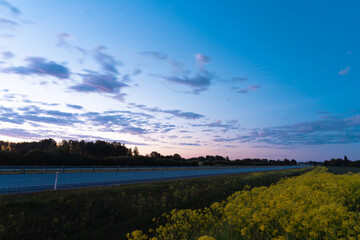 The highway at night against the background of the sunset sky. The yellow flowers in the foreground. Summer night.