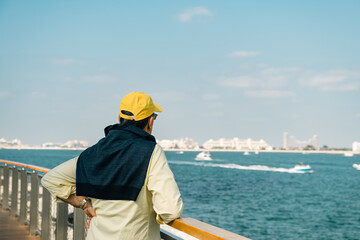 Fototapeta na wymiar Senior man looks at the sea while walking along the promenade next to the marina
