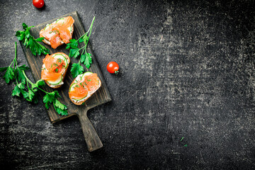 Salmon sandwich on a cutting board with herbs and tomatoes. 