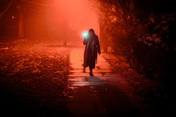 young woman walks through the city at night, illuminating the road with a cell phone flashlight - obrazy, fototapety, plakaty