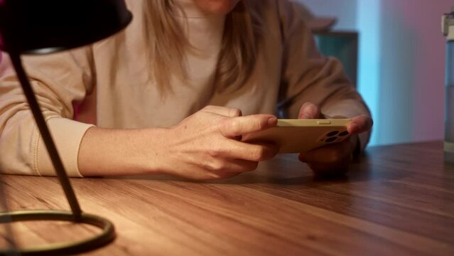 Close up cellphone. woman sits at table at home in headphones and play game on phone. neon light in room illuminates place of streamer or avid gamer girl. gamer is passionate playing on smartphone.