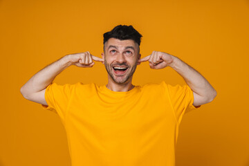 Fototapeta na wymiar Cheerful guy plugging his ears isolated over yellow background
