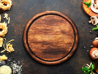 Uncooked pasta, brown champignons mushrooms, vegetables, cheese - ingredients for tasty cooking on old kitchen table background, dark style, top view