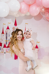 Photo portrait happy family: mother and daughter on balloons background. Woman and little baby girl princess. Concept of birthday celebration daughter is 1 year.