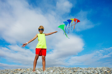 Smiling boy stand on pebble beach holding many colorful kites - Powered by Adobe