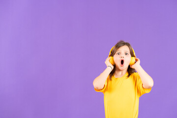 Surprised cute child listening to music on headphones isolated on purple background with copy space