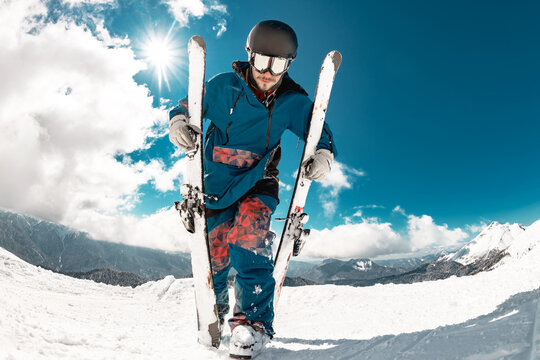 Happy young skier walks with ski in hands at mountain top. Ski resort concept