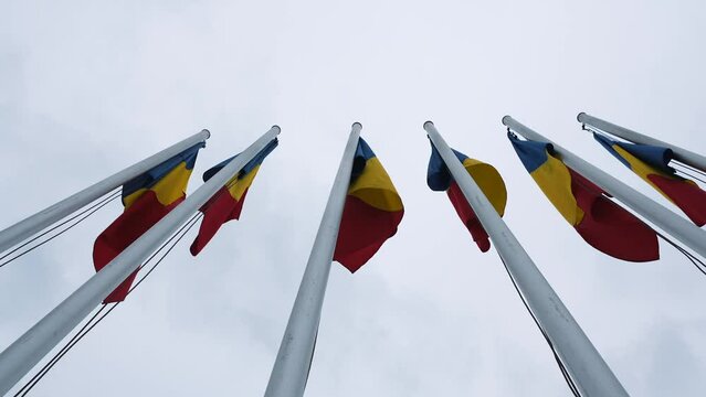 Flags of Romania waving in strong wind against cloudy sky, 4k video