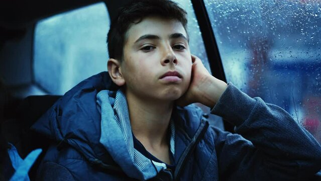 One bored teen boy seated in car backseat traveling during rainy day feeling boredom. Pensive contemplative kid