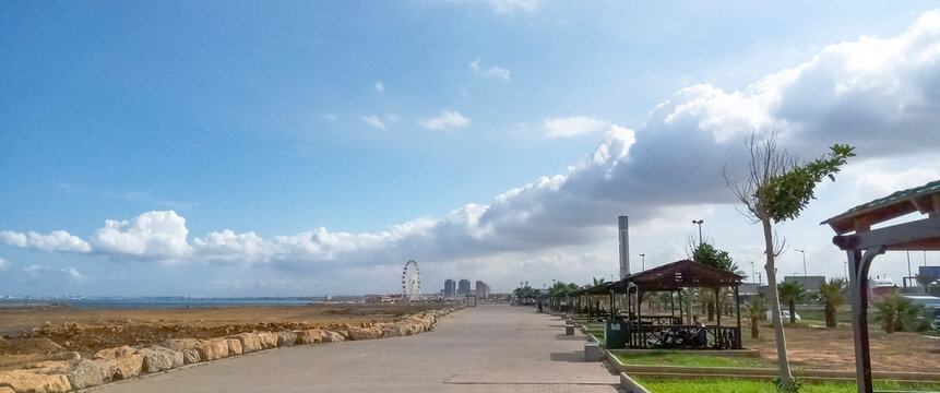 Sablettes promenade amusement park walkway in a sunny day with a big cloud in the shape of a sausage and a turn. The Algiers great mosque minaret, Ferris big wheel, buildings and sea bay.