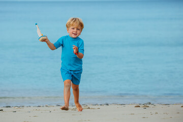 Fototapeta na wymiar Blond boy walk with boat toy model at the beach