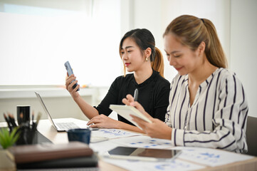 Fototapeta premium Attractive Asian businesswoman using her mobile phone while working with her coworker