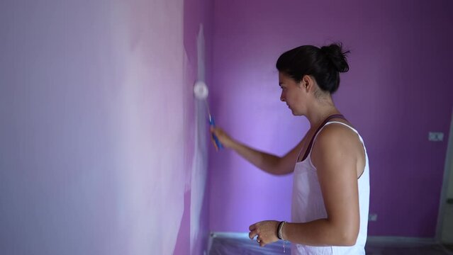 Person painting purple wall with white color. Woman doing house renovation paints new home. Female painter