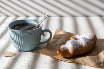 Cup of tea and croissants In striped morning sunlight. Breakfast tea with heart shaped label