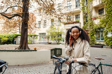 Smiling african girl in headphones standing with bicycle outdoors