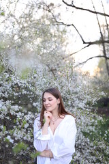 beautiful girl in a white shirt near a blooming tree. Beautiful warm spring and blossoming trees