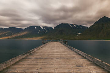 Long exposure landscape of wooden pier on the lake during cloudy day with high mountains and majestic sky on the background
