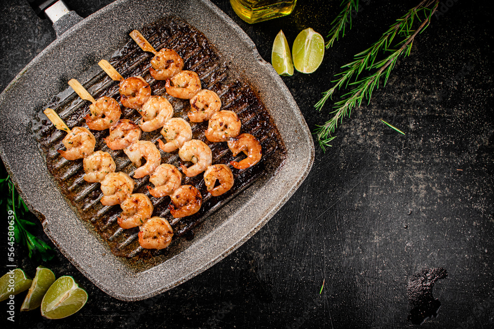 Poster Grilled shrimp on skewers in a frying pan with rosemary and pieces of lime. 