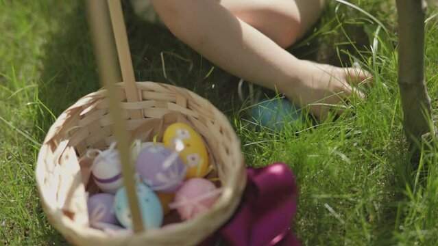 Happy Easter egg hunt game concept child's hands pick up colorful Easter eggs put them into basket. Sunny warm spring daytime holiday outdoors. Easter holiday for children and families