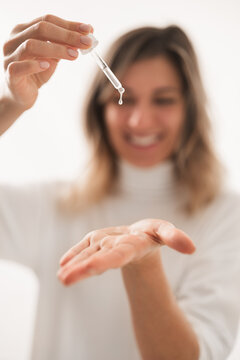 Cheerful young woman applying serum on hand and smiling